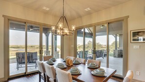 A dining area with a large table set for six, surrounded by chairs, with a view through glass doors to an outdoor patio. - Elegant 'sunset Meadow Ranch' in Texas w/ Hot Tub (Ponder)