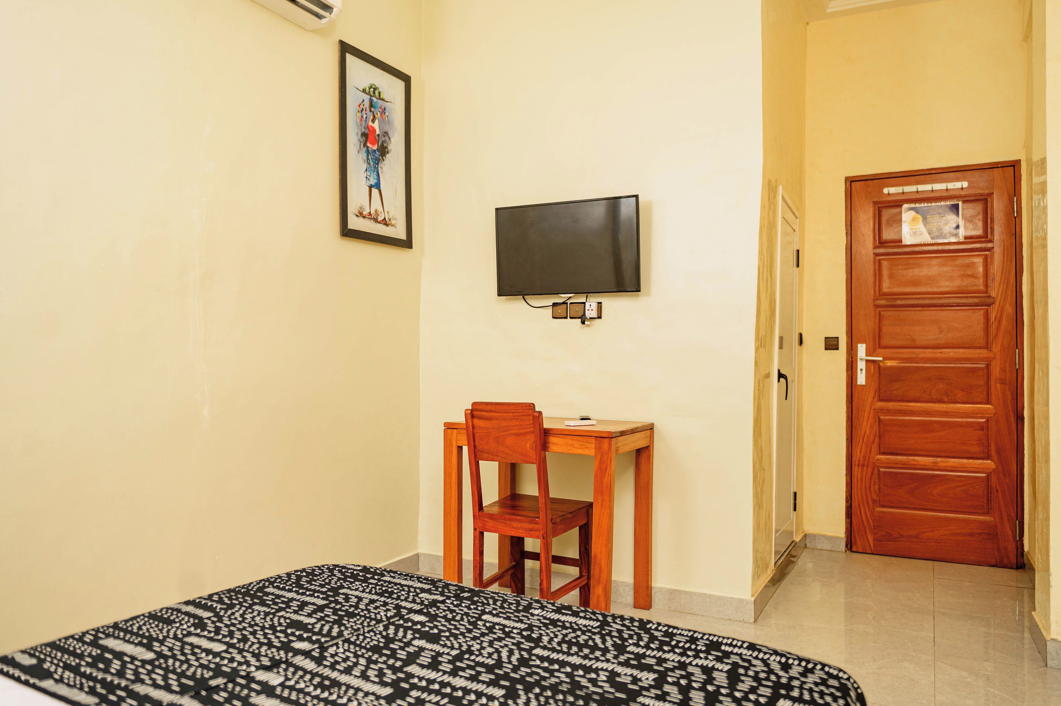 A room with a bed, a desk with a chair, a television mounted on the wall, and a wooden door.