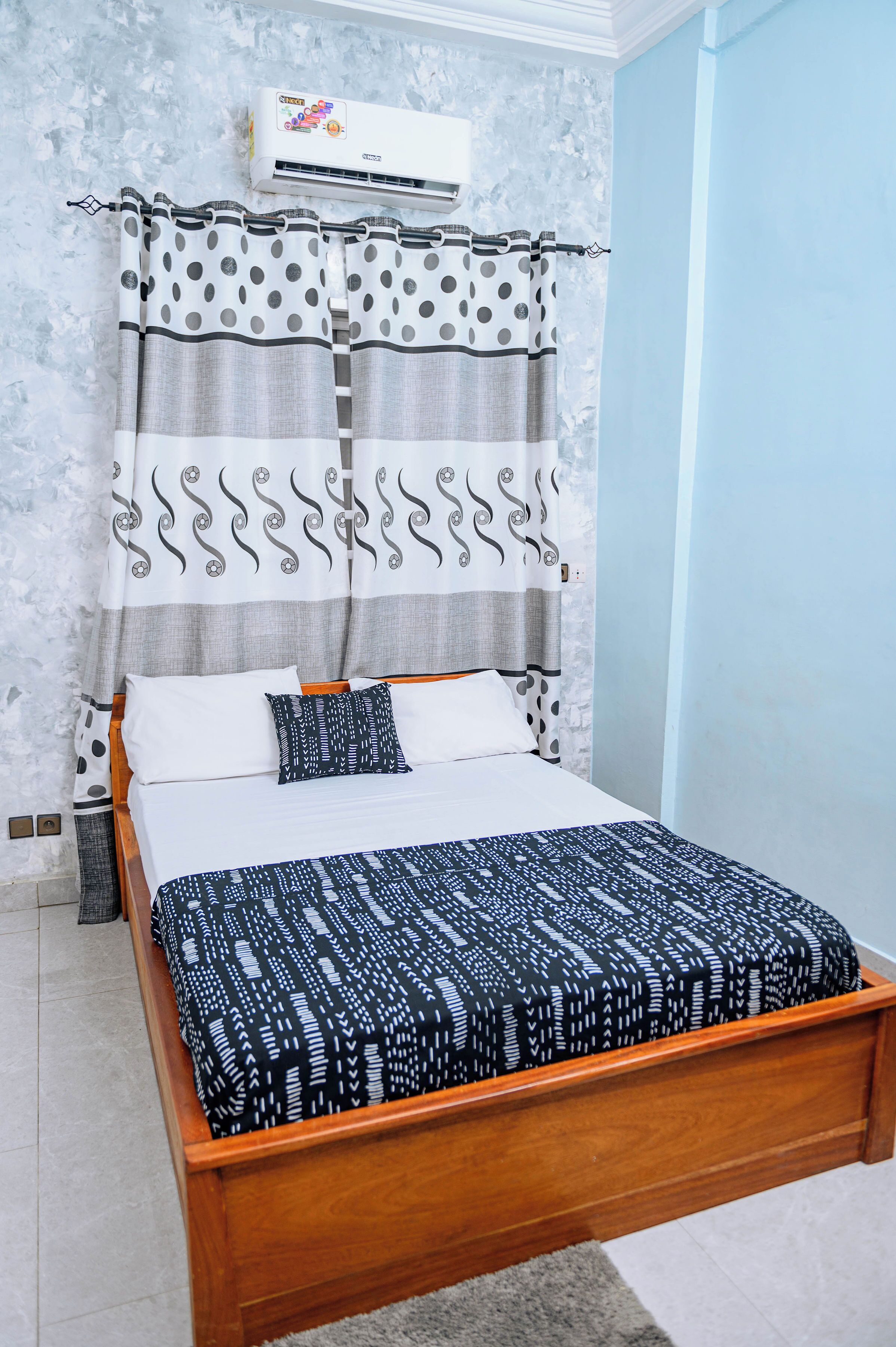 A bed with a patterned bedspread, a headboard with curtains, and an air conditioning unit above.