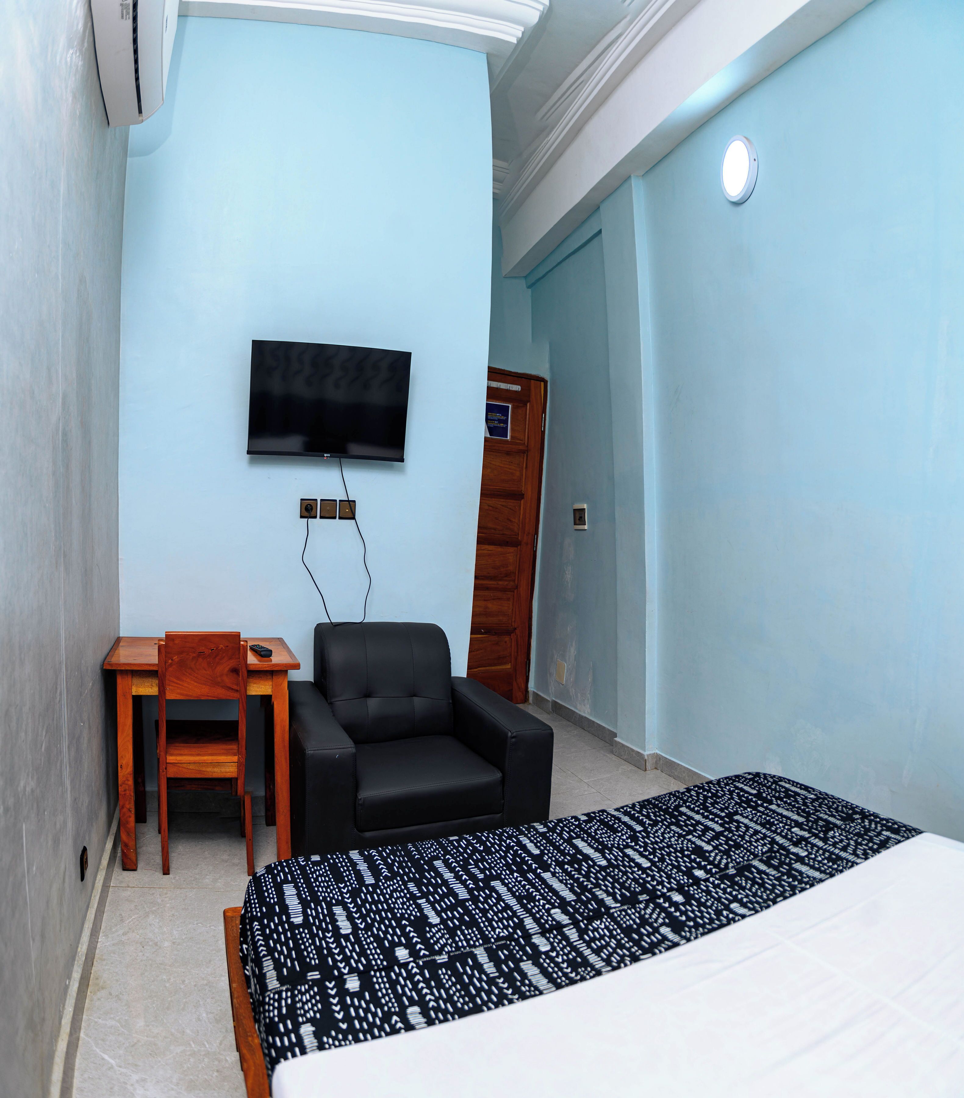 Una habitación de hotel con cama, escritorio, silla, televisor montado en la pared y puerta.