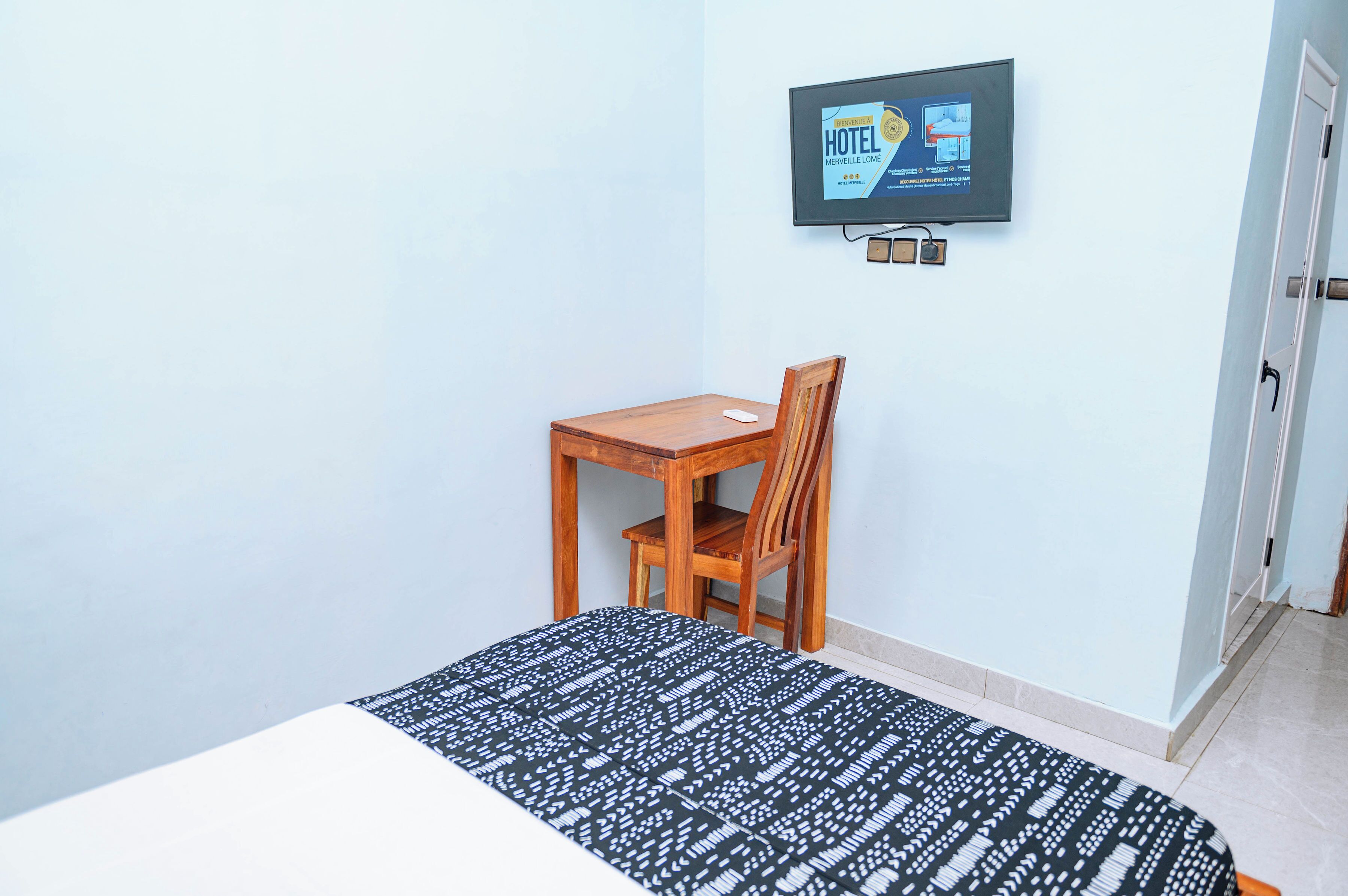 Een hotelkamer met een bed, een houten stoel, een bureau en een aan de muur bevestigde televisie.
