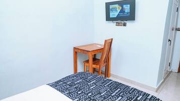 Een hotelkamer met een bed, een houten stoel, een bureau en een aan de muur bevestigde televisie.