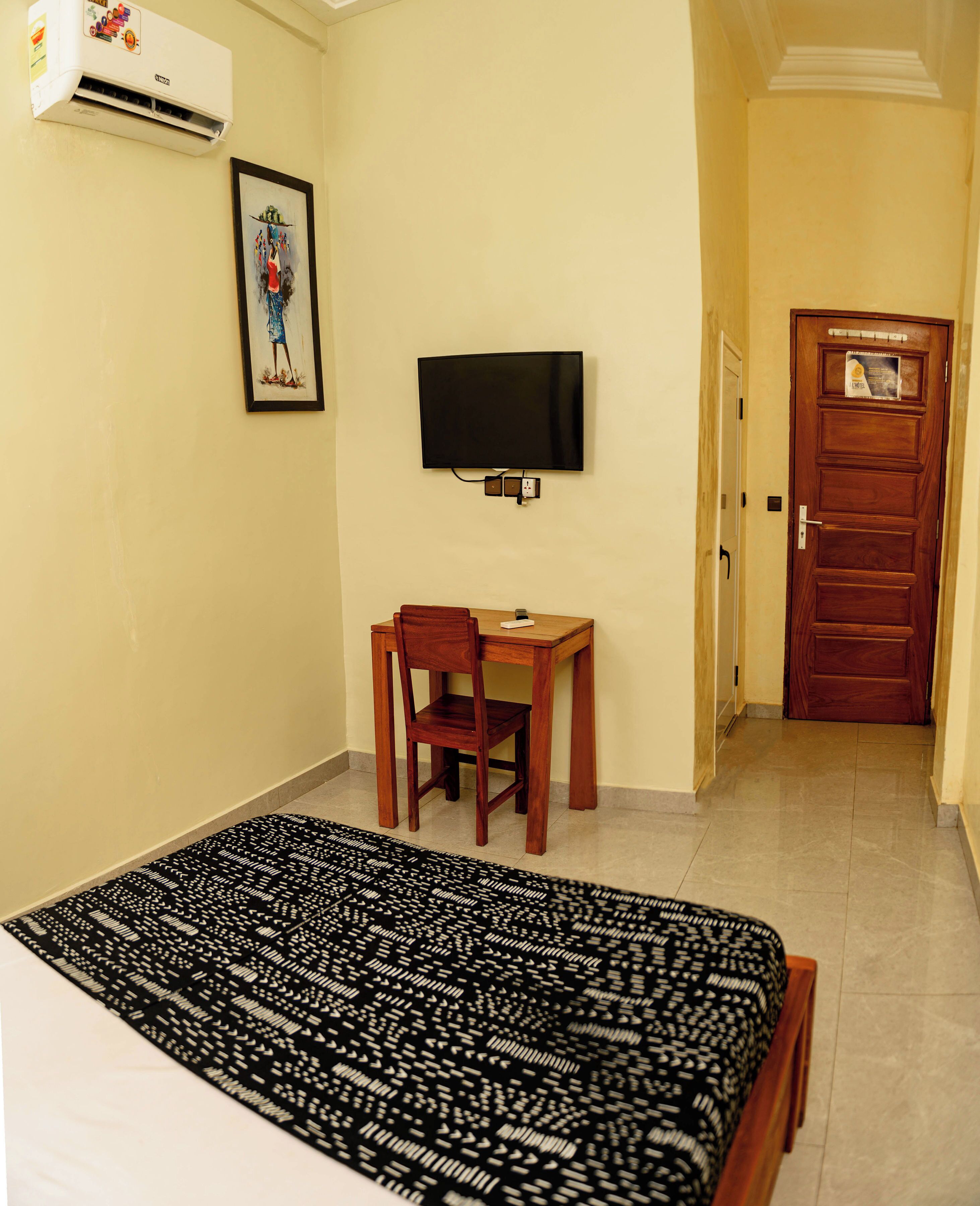 A hotel room with a bed, a desk, a chair, a television, and an air conditioning unit.