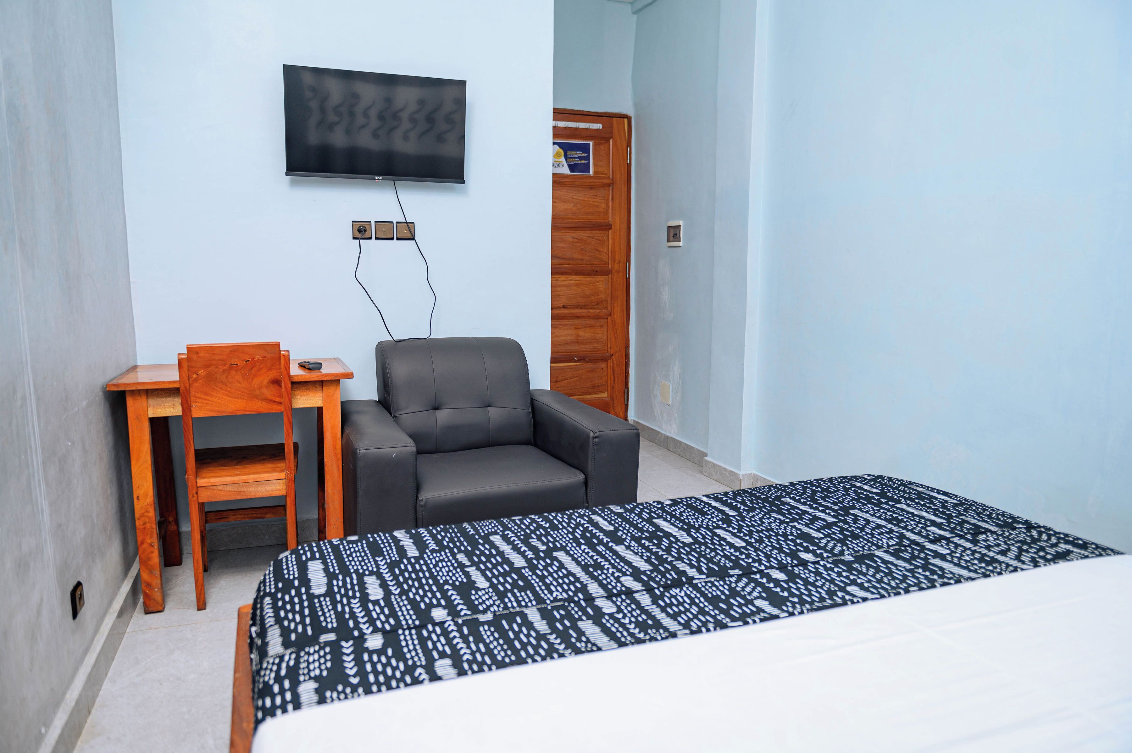 Quarto com cama, escrivaninha, cadeira, televisão e porta.
