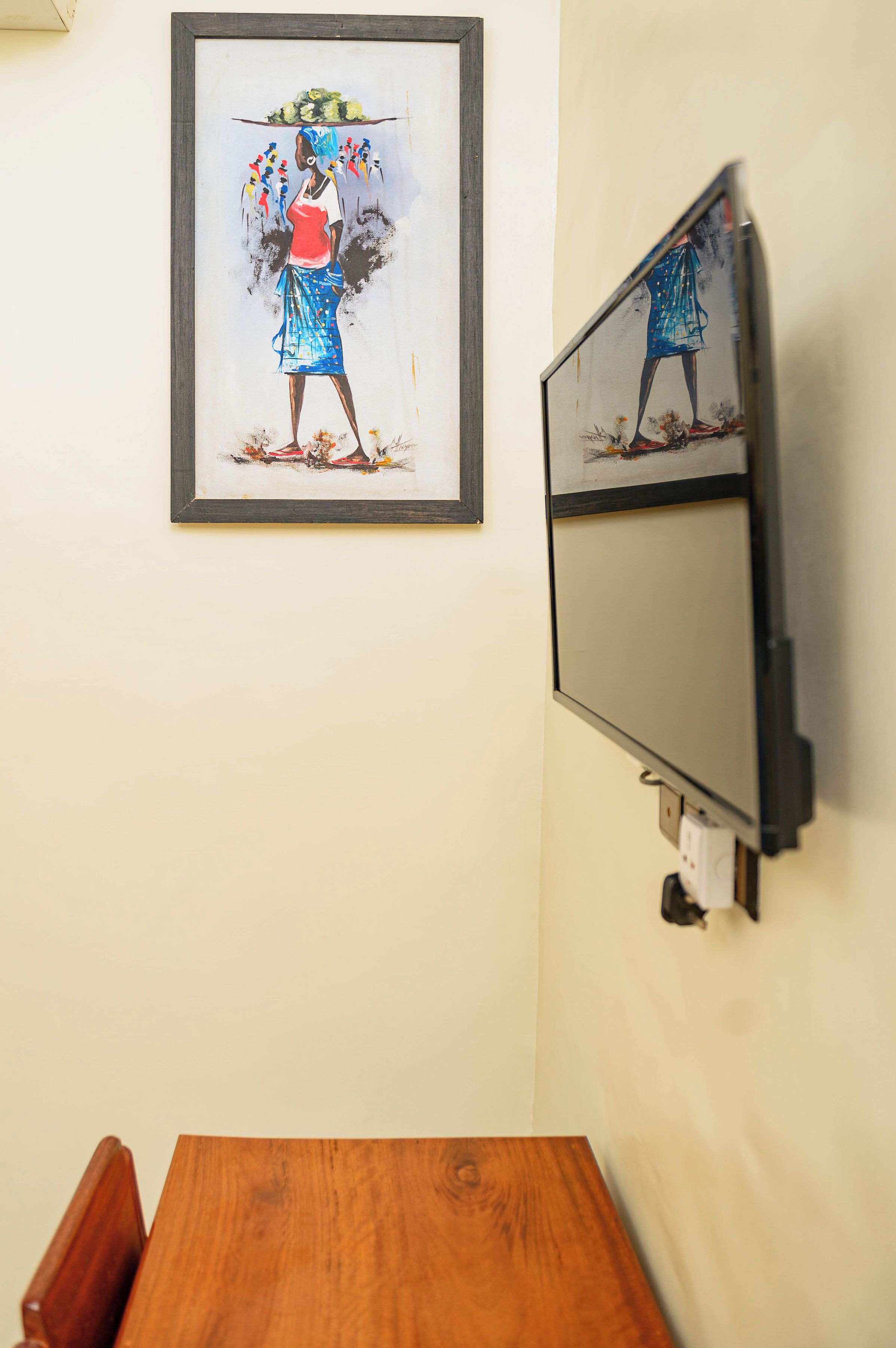 Un tableau encadré représentant une femme vêtue d’un costume traditionnel, un téléviseur fixé au mur et une table en bois.