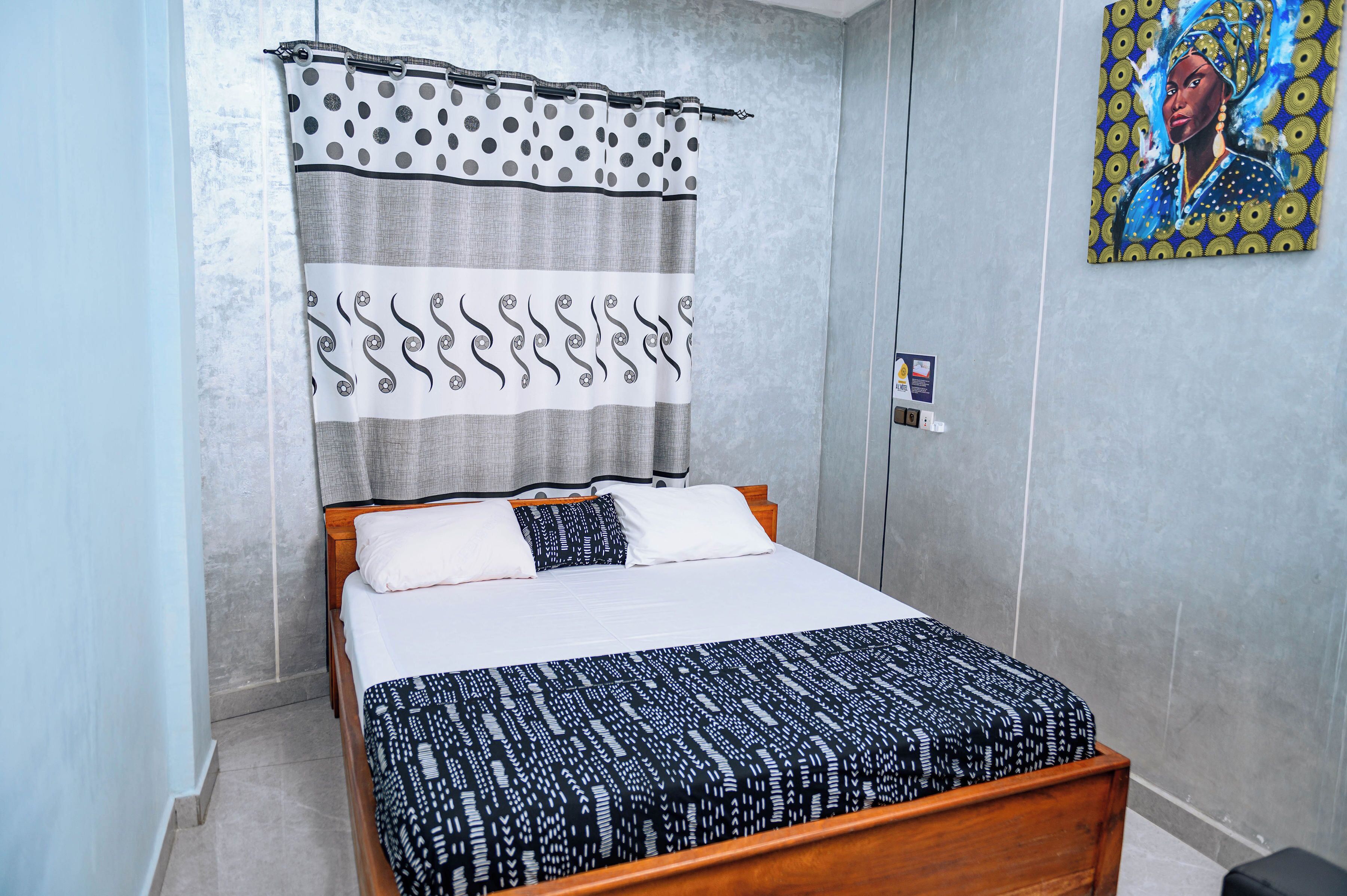 A bedroom with a bed, a curtain, a painting on the wall, and a small sign.