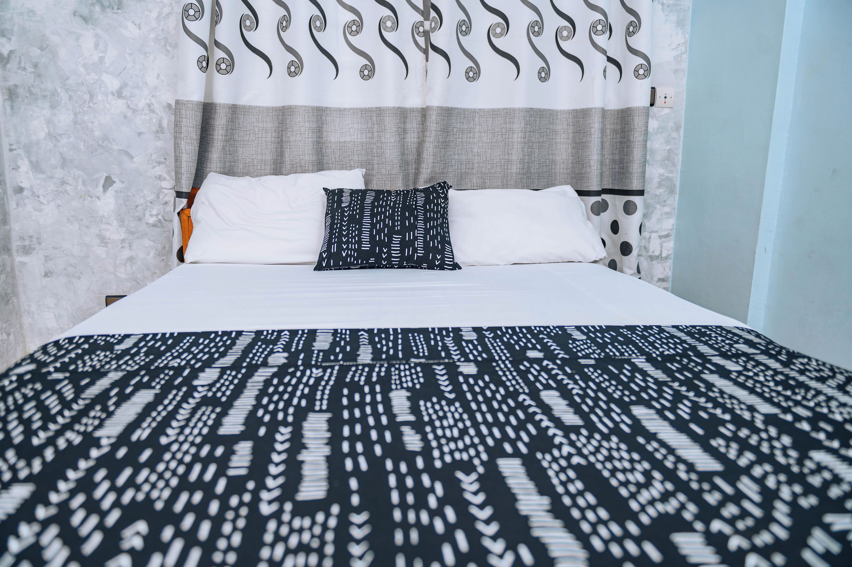 A bed with white and patterned bedding, a grey headboard, and a curtain with a soccer ball pattern.