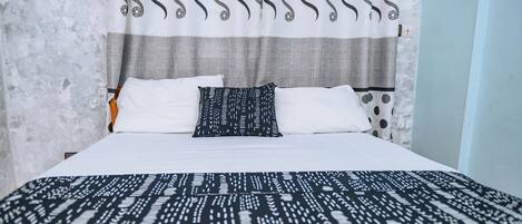 A bed with white and patterned bedding, a grey headboard, and a curtain with a soccer ball pattern.