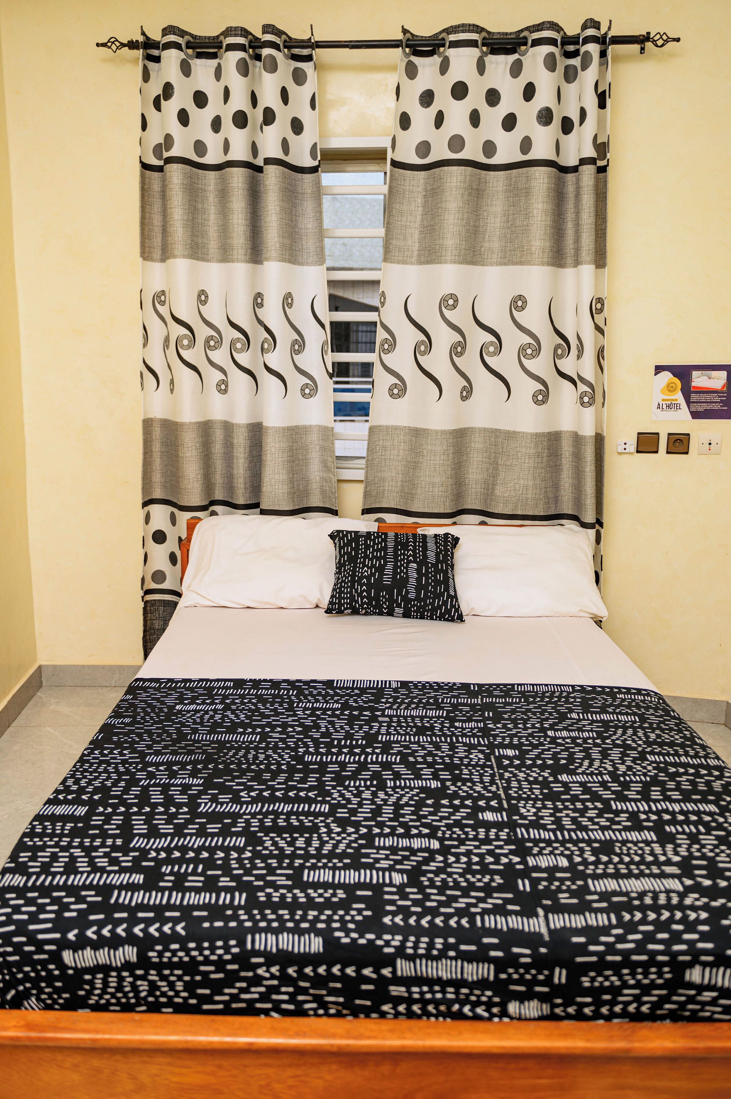 Una habitación de hotel con una cama, cortinas, un almohadón y un cartel en la pared.