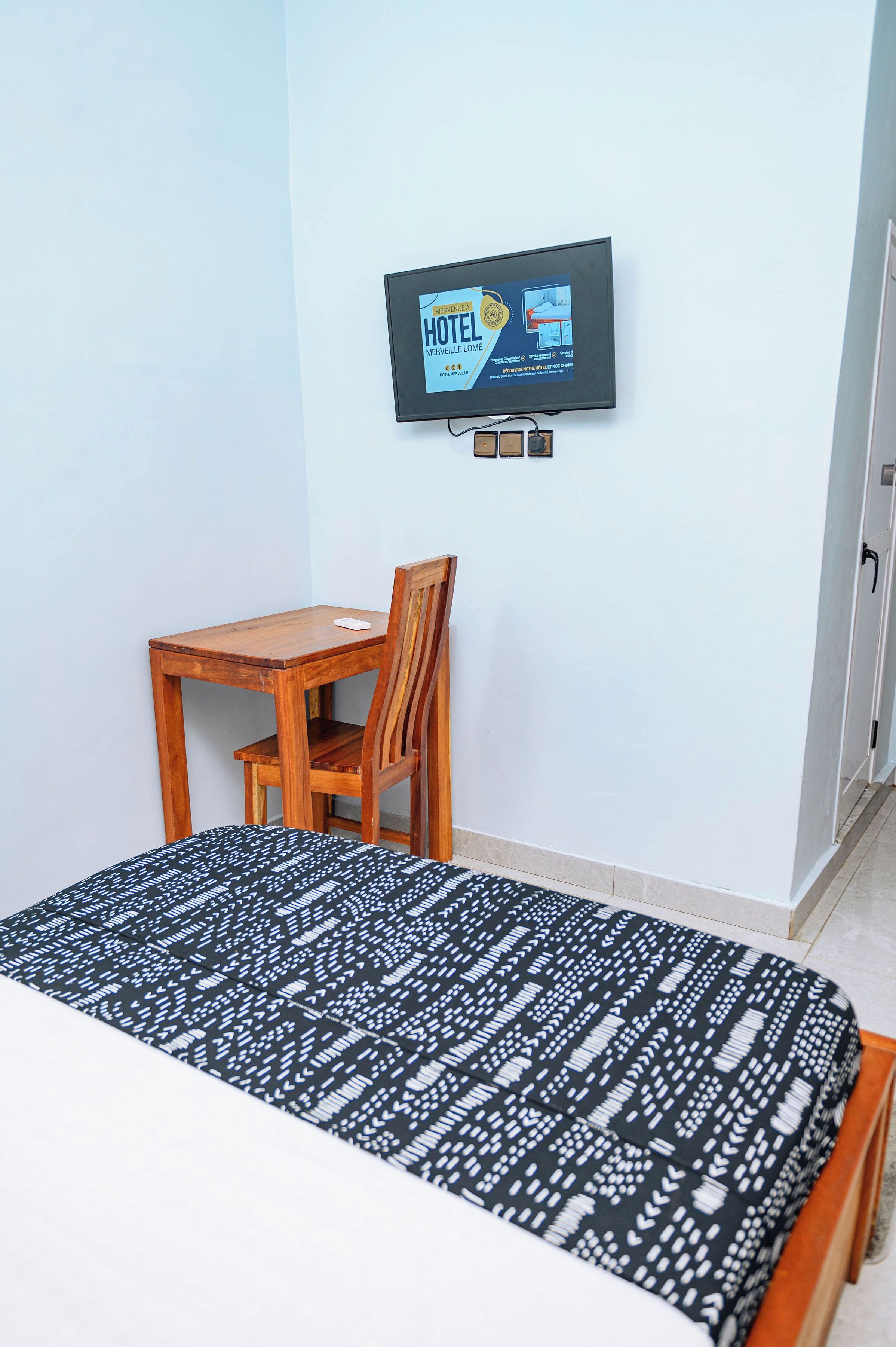 Une chambre d’hôtel avec un lit, une chaise en bois, un téléviseur fixé au mur et une petite table.
