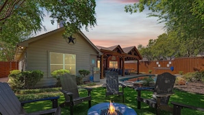 A backyard with a fire pit, outdoor seating, a swimming pool, and a house with a star on the wall.