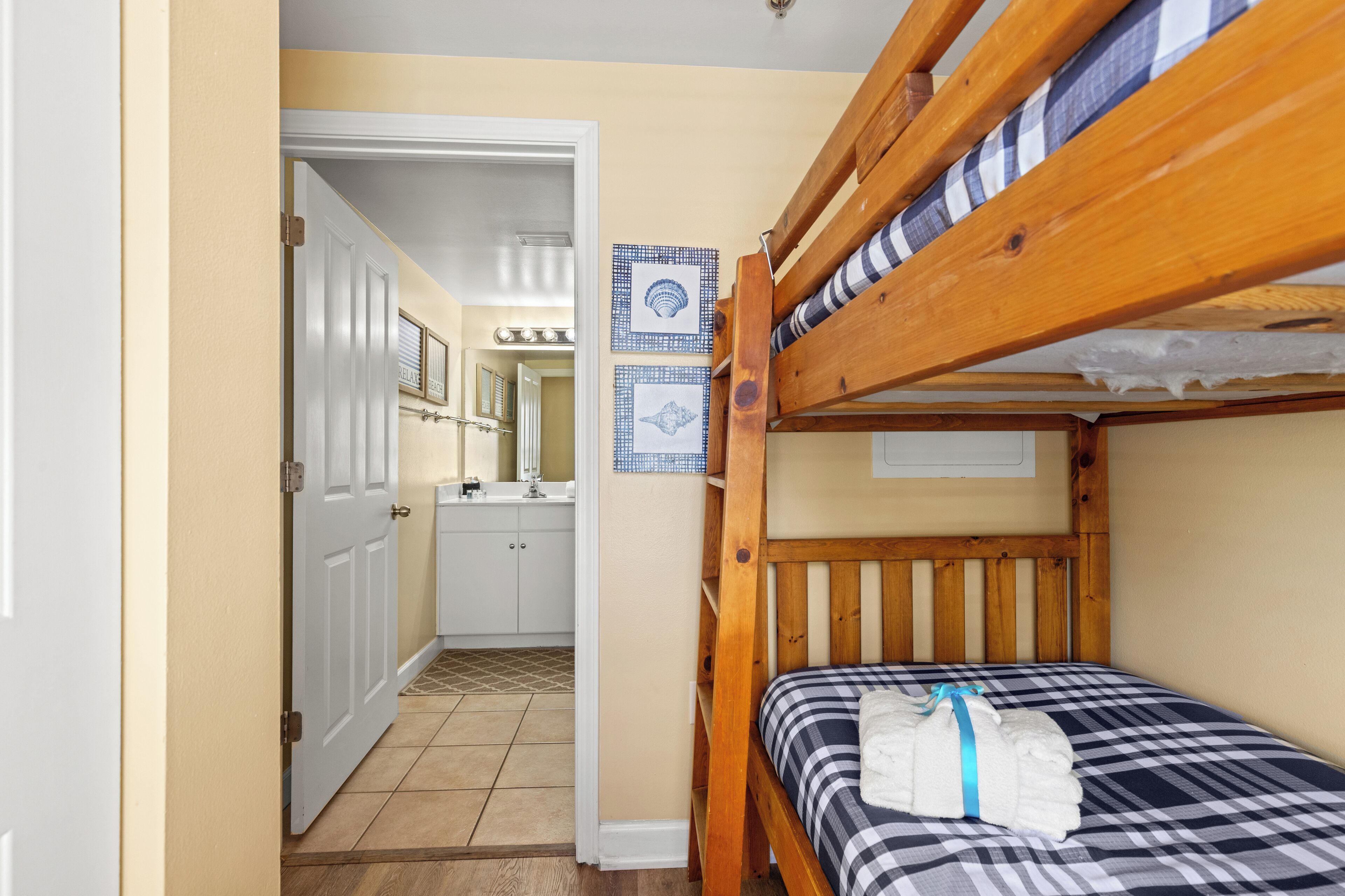 A small, compact room with a bunk bed, a bathroom with a sink and mirror, and a door leading to another room.
