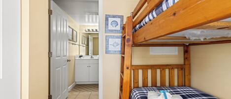 A small, compact room with a bunk bed, a bathroom with a sink and mirror, and a door leading to another room.
