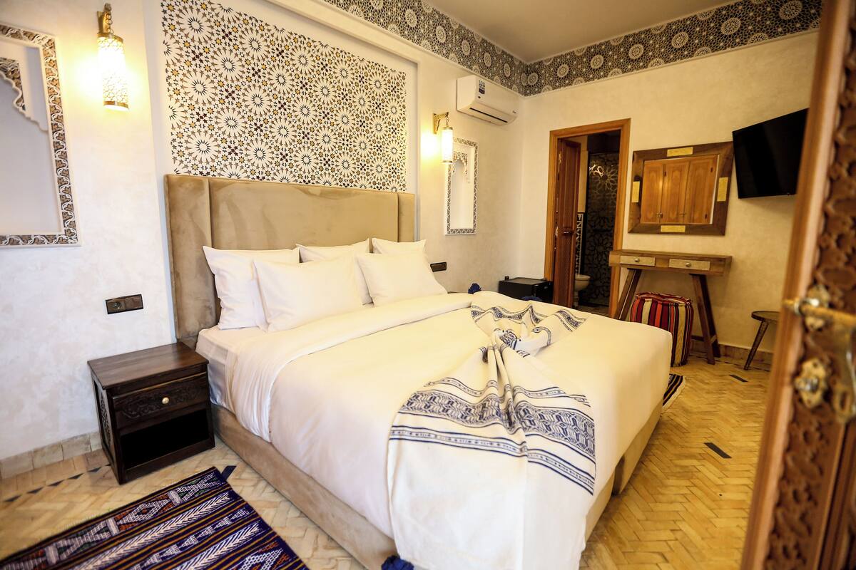 Une chambre d’hôtel avec un grand lit, une table de chevet, un téléviseur fixé au mur et une tête de lit à motifs.