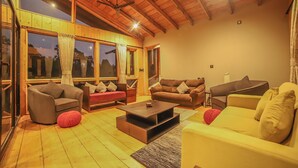A cozy living room with wooden floors, a ceiling fan, and large windows. - Triptych by Xplore Indo (Kotagiri)