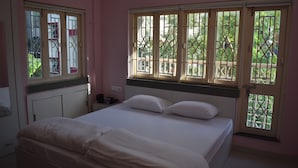 A bedroom with a bed, a nightstand, and a window with a view of greenery. - Bonussa Homestay (Kolkata)