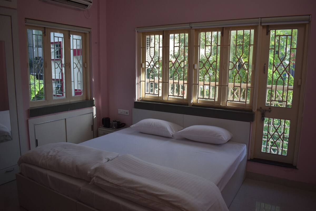 A bedroom with a bed, a nightstand, and a window with a view of greenery.