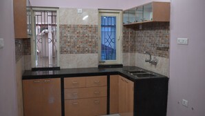 A kitchen with a black countertop, wooden cabinets, a sink, and a window with a metal gate. - Bonussa Homestay (Kolkata)