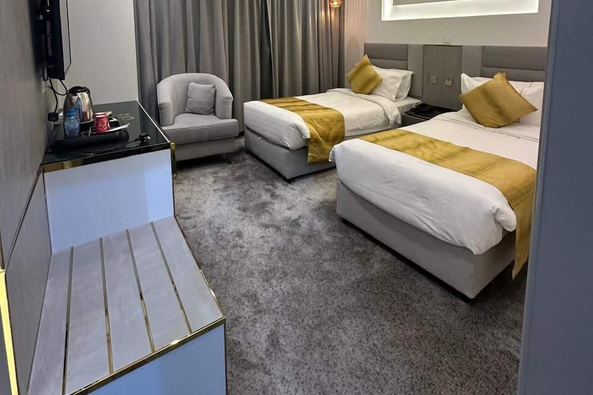 A modern hotel room with two beds, a sofa, a desk, and a television.