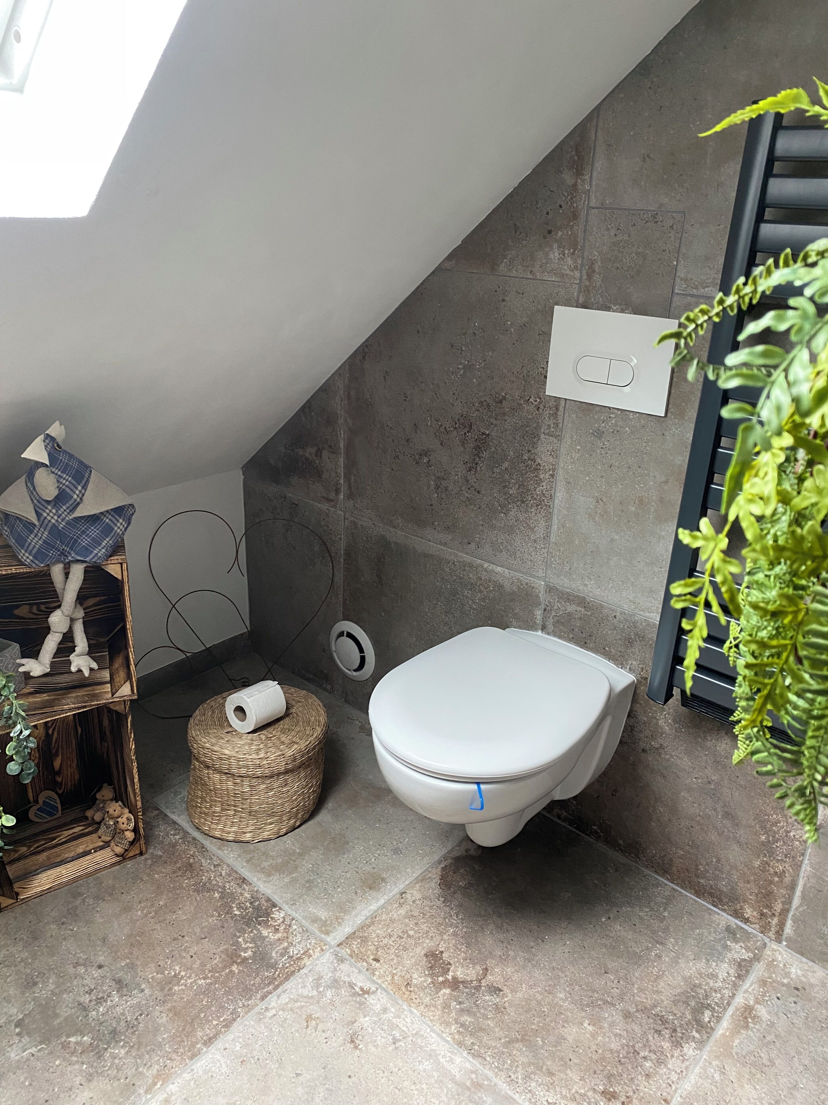 Ein Badezimmer mit Toilette, einem kleinen Korbwäscheschrank, einer Deko-Fischfigur und einer Pflanze.