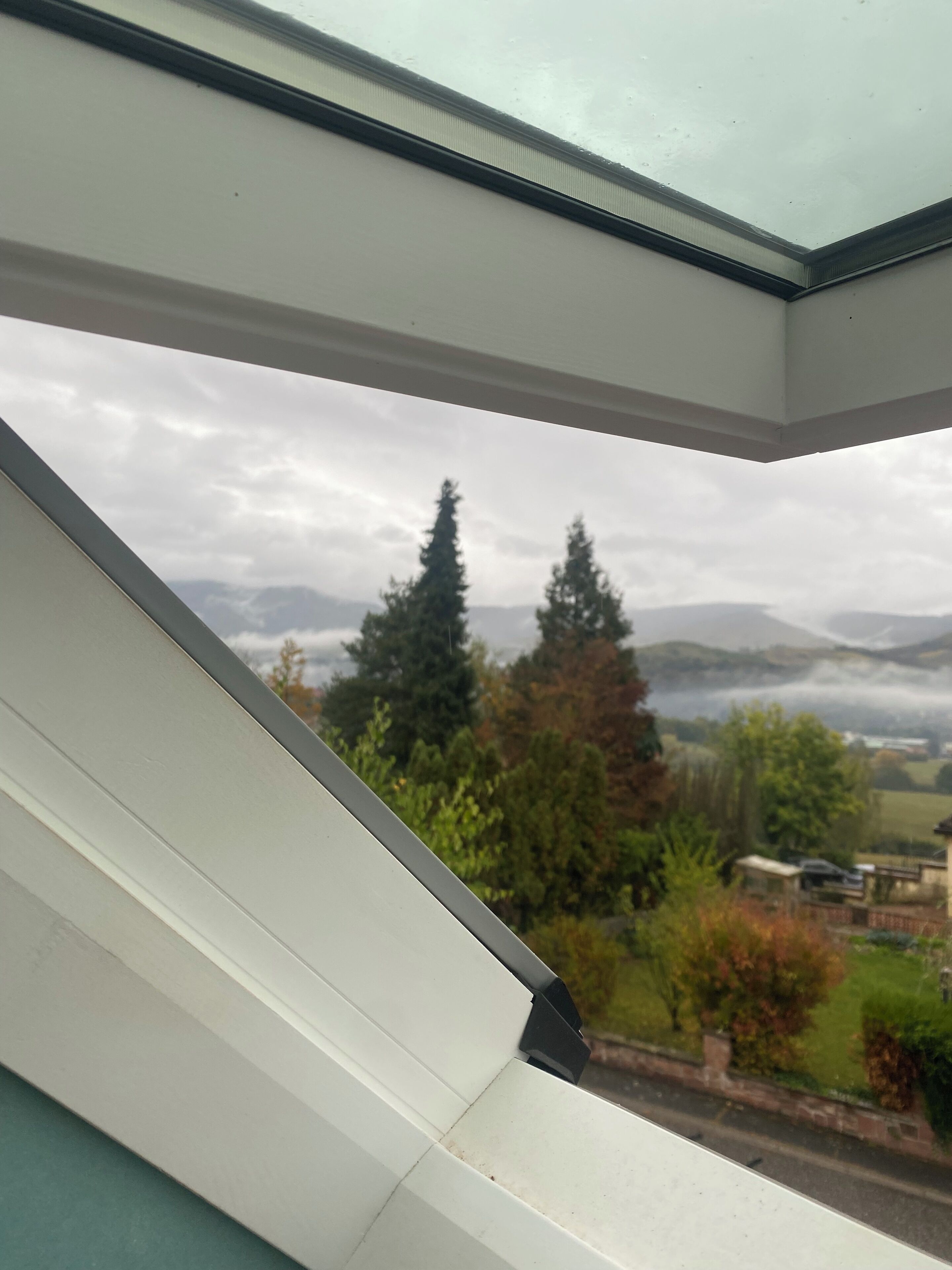Vista a través de una ventana de marco blanco, que da a un paisaje con árboles y montañas lejanas.