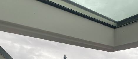 Vista a través de una ventana de marco blanco, que da a un paisaje con árboles y montañas lejanas.