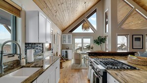 Una cocina moderna con una isla grande, techo de madera y ventanas amplias.
