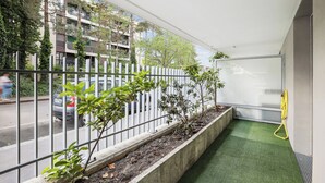 A balcony with a green artificial turf floor, a white metal railing, and a concrete planter with small plants. - Apart-Chic-Les-Ulis with terrace and parking. (Les Ulis)