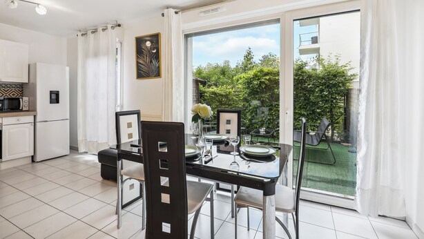 A modern kitchen with white cabinets and a dining area with a glass table and chairs. - Apart-Chic-Les-Ulis with terrace and parking. (Les Ulis)