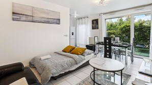 A modern bedroom with a bed, a small round table, and a balcony with a view of greenery. - Apart-Chic-Les-Ulis with terrace and parking. (Les Ulis)
