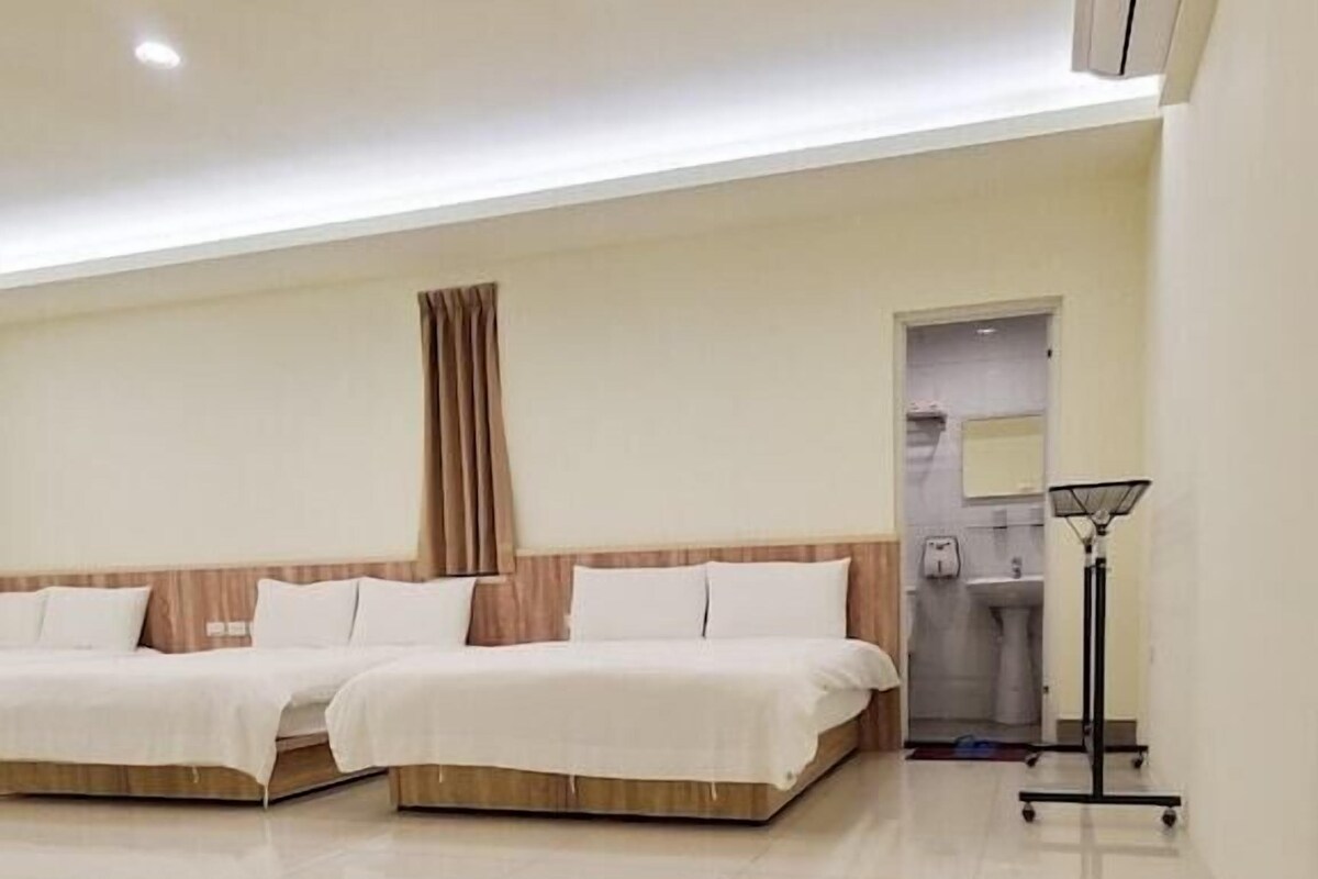 A hotel room with two beds, a bathroom, and a standing lamp.