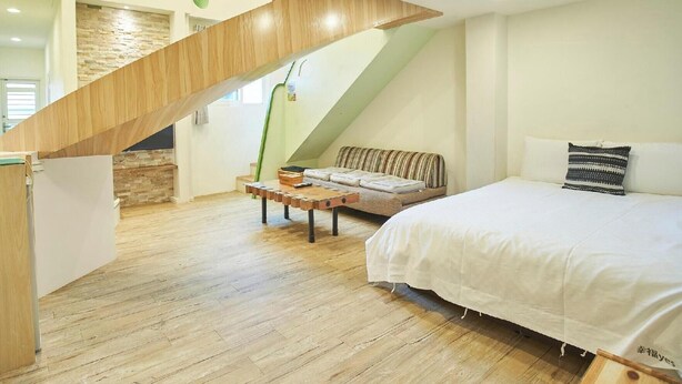 A bedroom with a wooden staircase, a bed with white bedding, and a small seating area with a bench and cushions. - Happiness YES (Yilan)