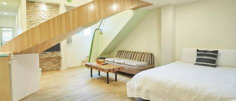A bedroom with a wooden staircase, a bed, a sofa, and a small table.
