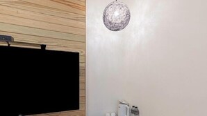 A modern room with a flat-screen TV mounted on a wooden wall, a small table with a coffee maker and water bottles, and a compact refrigerator. - Happiness YES (Yilan)