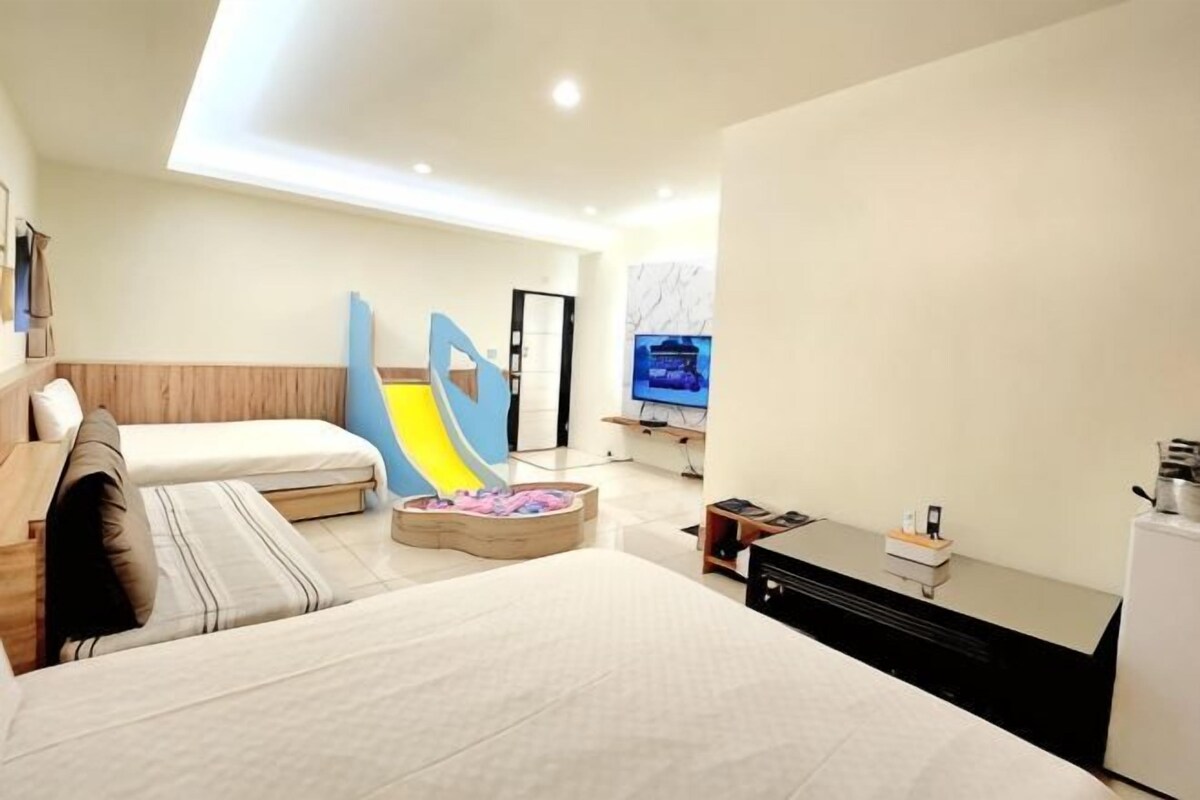 A modern hotel room with a bed, a sofa, a TV, and a small play area.
