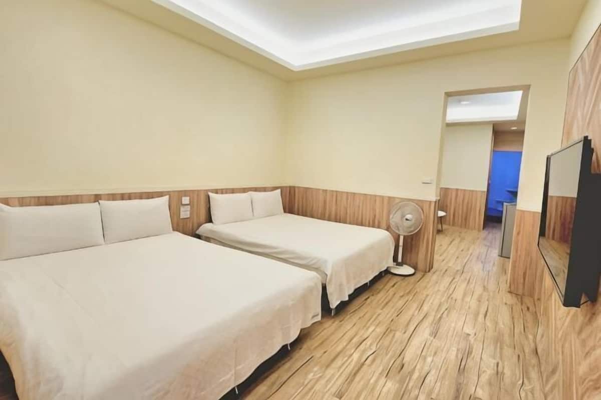 Hotellihuone, jossa on kaksi sänkyä, kattotuuletin, peili ja puulattia.