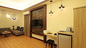 A compact living space with a sofa, a small table, a TV mounted on a brick wall, a kitchenette with a refrigerator, and a wooden cabinet. - Happiness YES (Yilan)