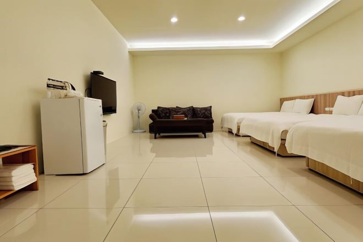 A hotel room with a bed, a sofa, a TV, a refrigerator, and a bedside table.
