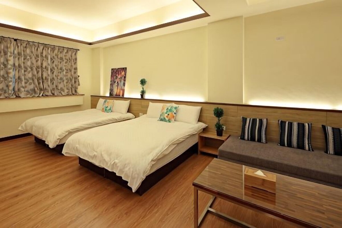 A hotel room with two beds, a sofa, a wooden coffee table, and a small table with a plant.