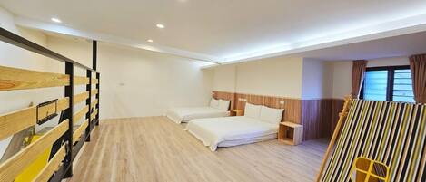 A hotel room with a wooden floor, two beds, a wooden bunk bed, a striped partition, and a window with curtains.