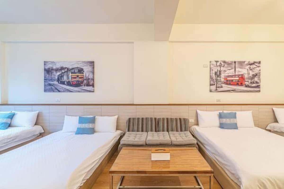 Hotellihuone, jossa on kaksi sänkyä, sohva, puinen sohvapöytä ja kaksi seinälle ripustettua taideteosta.