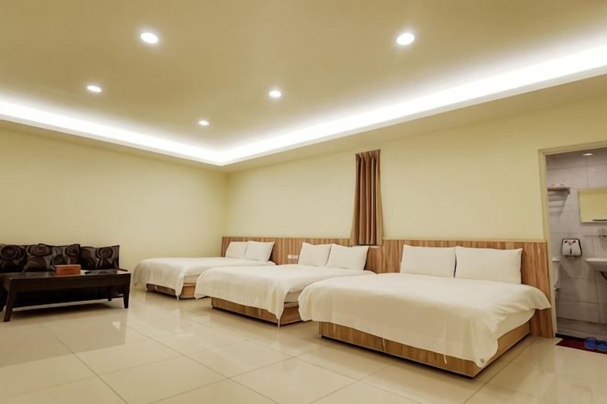 A hotel room with three beds, a sofa, a small table, and a bathroom visible through an open door.