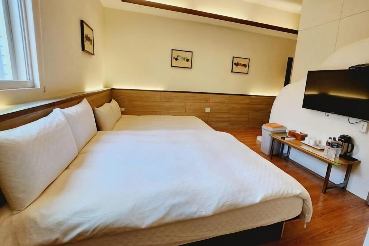 A hotel room with a large bed, a wooden headboard, a television, and a small table with a coffee maker.