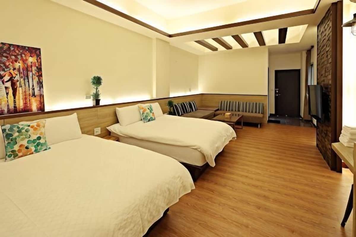 Hotellihuone, jossa on kaksi sänkyä, sohva, televisio ja taulu seinällä.