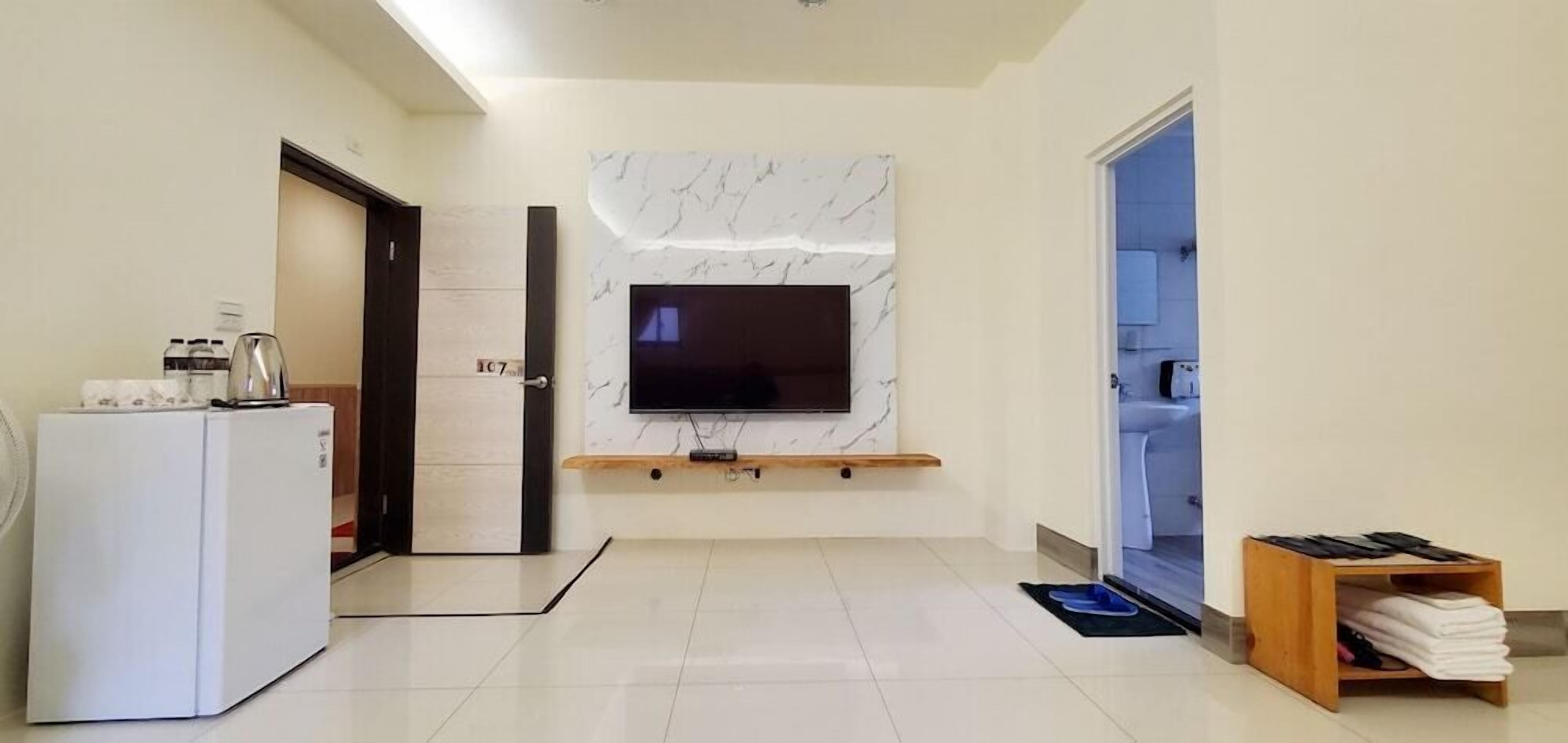 A modern living room with a flat-screen TV mounted on a marble wall, a white refrigerator, and a wooden shelf.