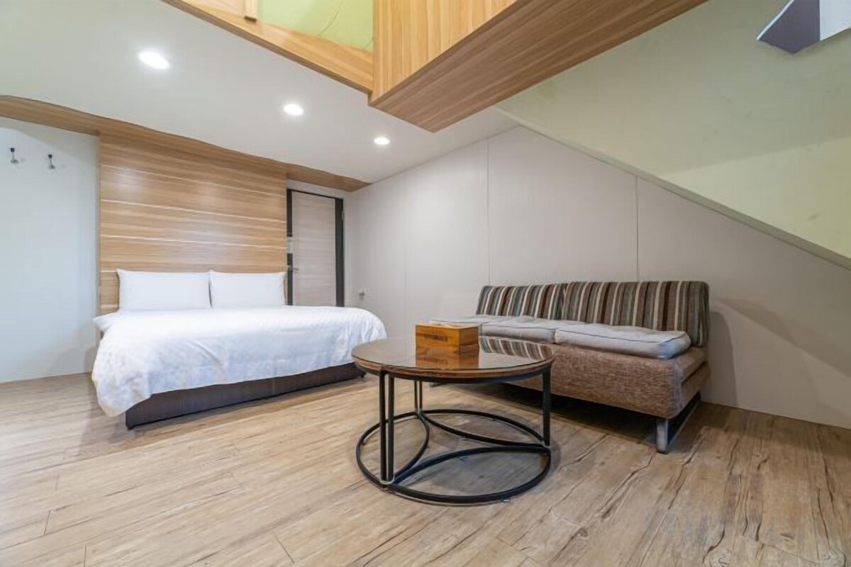 A bedroom with a bed, a sofa, a round table, and a sloped ceiling.