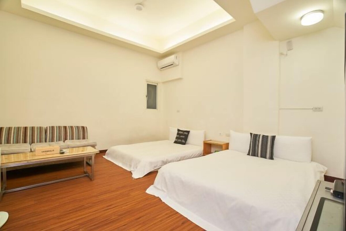 A hotel room with two single beds, a sofa, a small table, and a ceiling light.