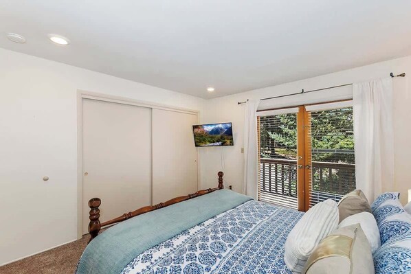 A bedroom with a bed, a television, a sliding glass door to a balcony, and a white door.