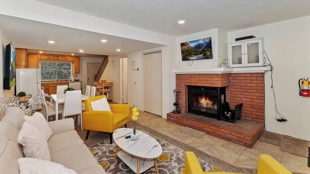 A living room with a fireplace, yellow armchairs, a white sofa, and a dining area with a table and chairs. - Snowy Pines | Walk to Snow Summit · Fireplace (Big Bear Lake)
