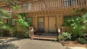 A two-story building with a wooden balcony, a front door, and a small porch area. - Snowy Pines | Walk to Snow Summit · Fireplace (Big Bear Lake)